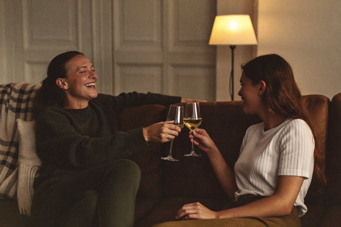 Två kvinnor skålar med vitt vin i en soffa